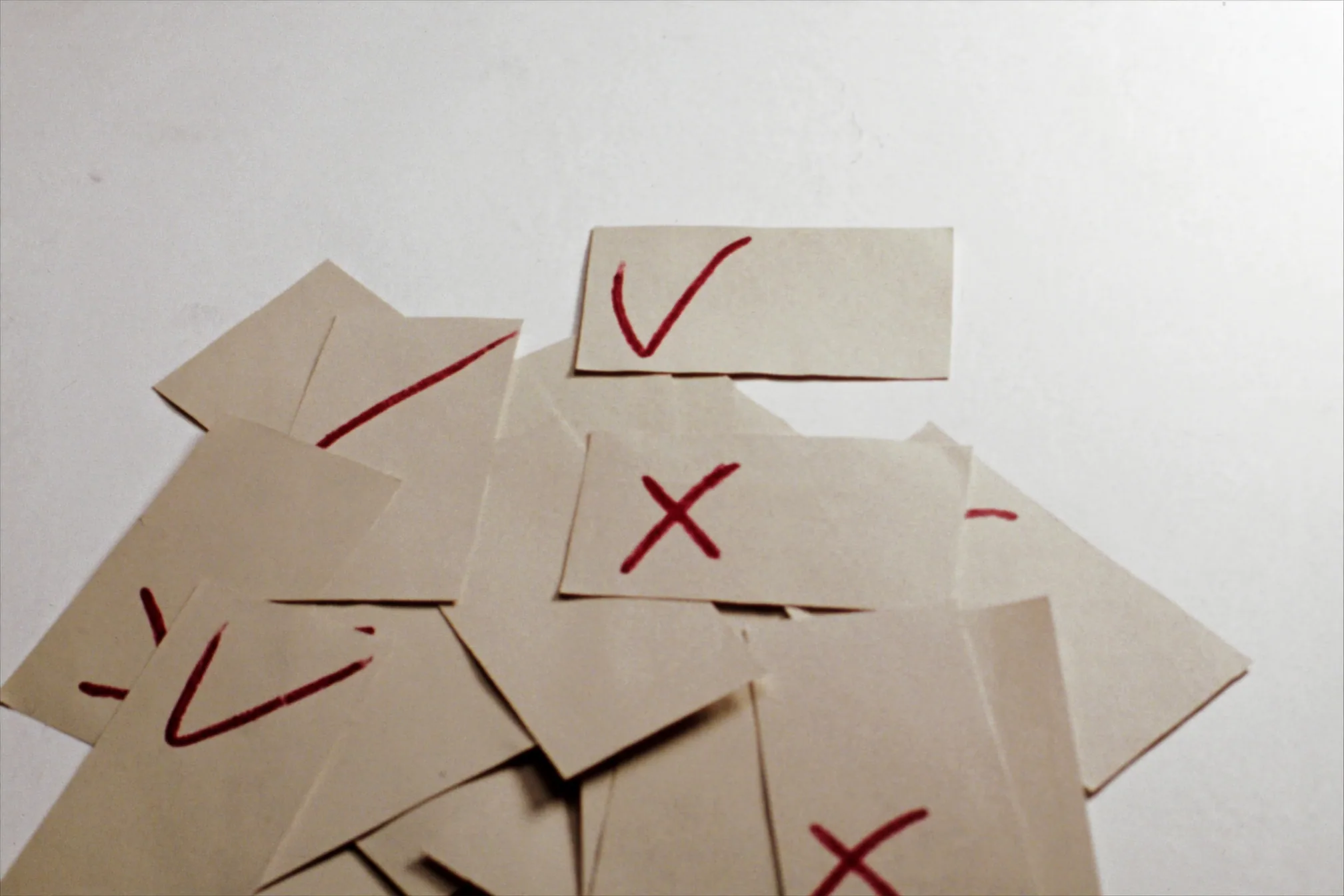 Small paper cards scattered on a white surface, each marked by hand with a red tick or cross.